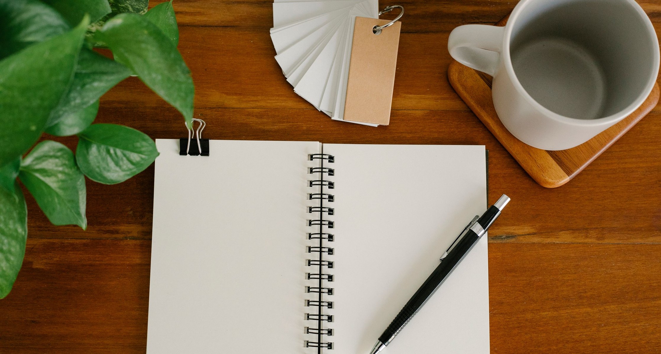 Aufgeschlagenes leeres Notizbuch mit Stift, Tasse und Pflanze von oben auf einem Holztisch